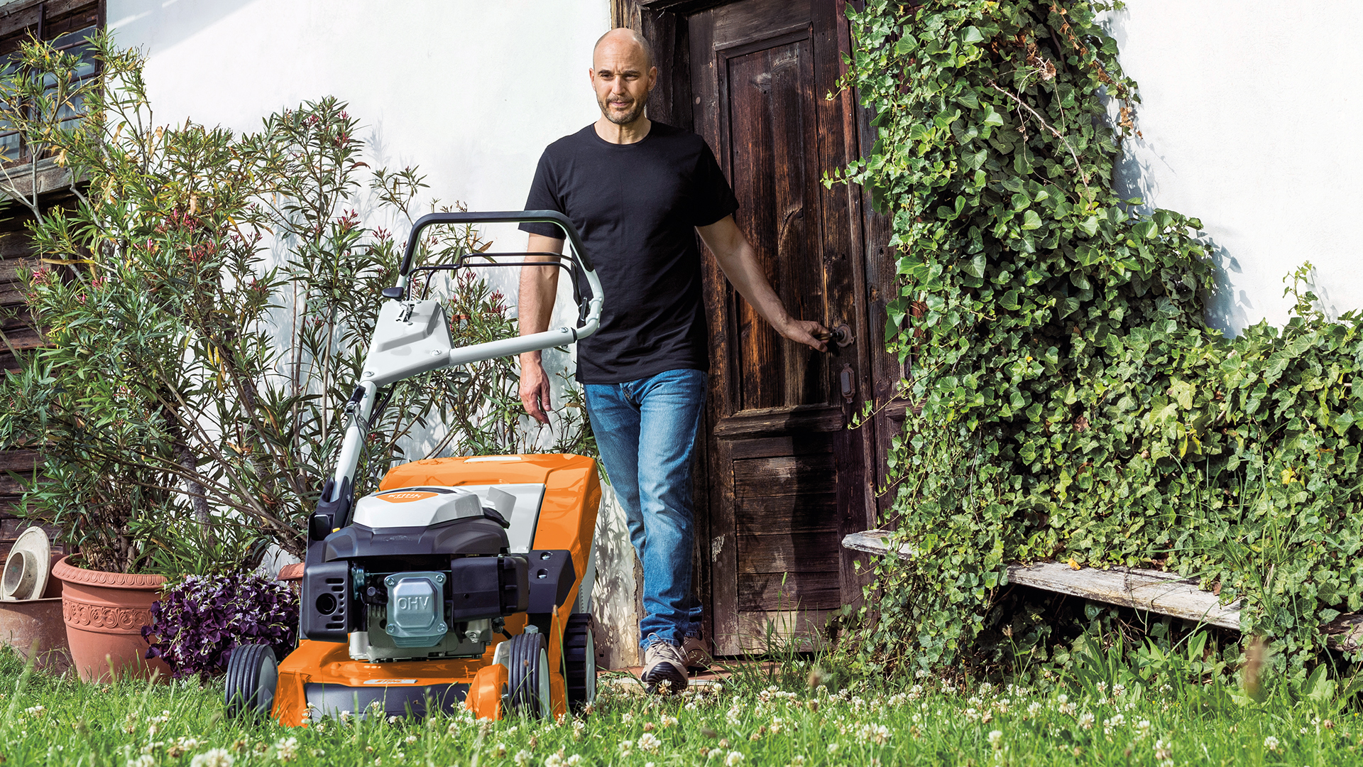 Mann geht von Tür in den Garten zu einem STIHL Benzin-Rasenmäher RM 650