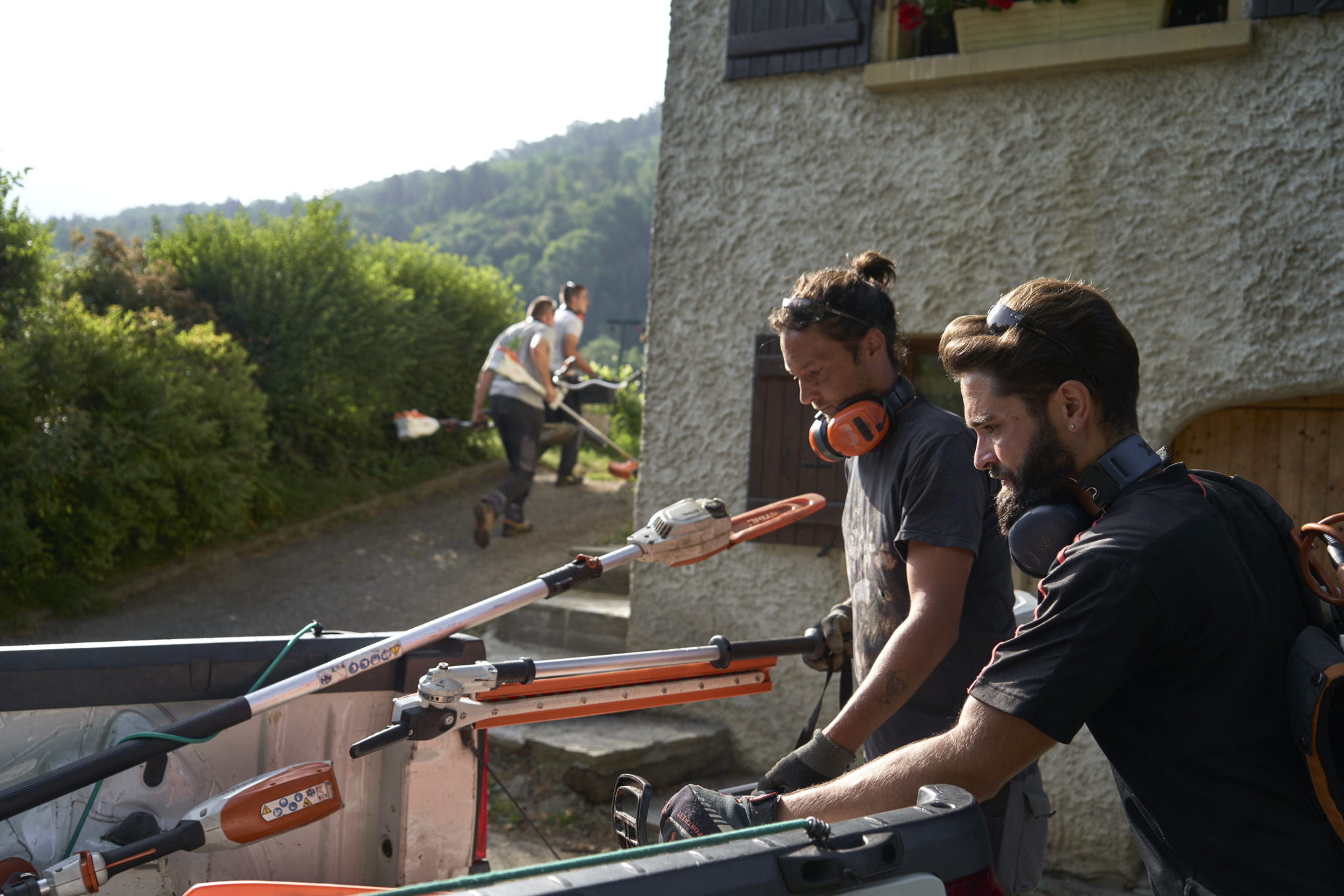 Dvojica pejzažnih arhitekti istovaruju STIHL baterijske uređaje iz automobila, a ostali radnici se vide u pozadini 