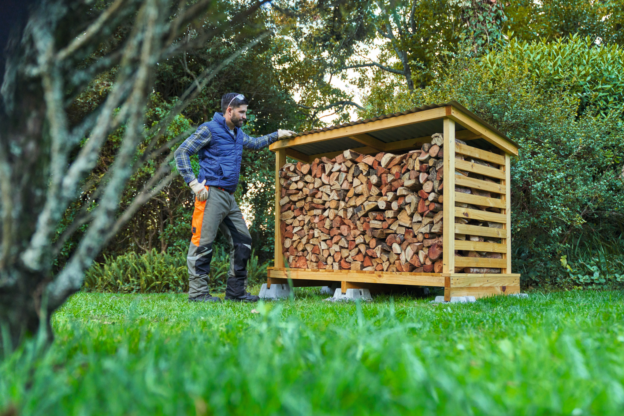 Muškarac u zaštitnoj opremi ispred drvenog skloništa koje je sam napravio