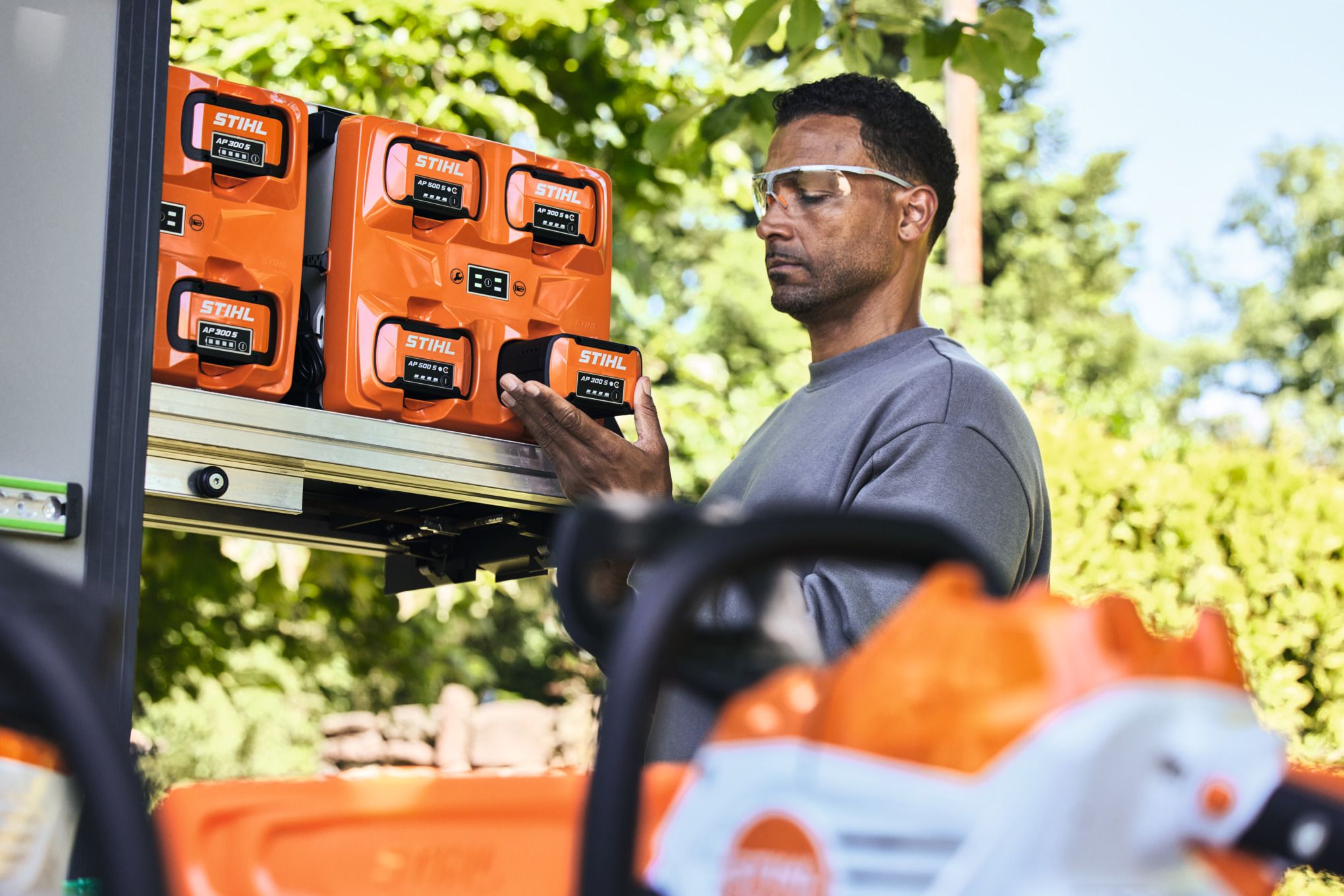 Muškarac sa zaštitnim naočarima uzima bateriju STIHL AP 300 S iz bottTainer-a