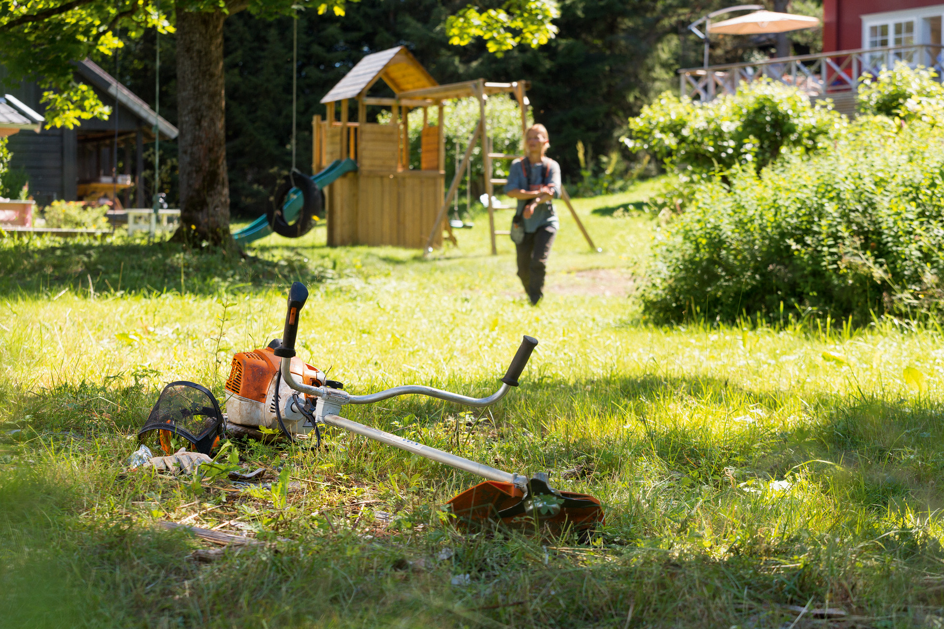 Motorna kosa STIHL FS 240 leži u travi, u pozadini se žena priprema za održavanje 