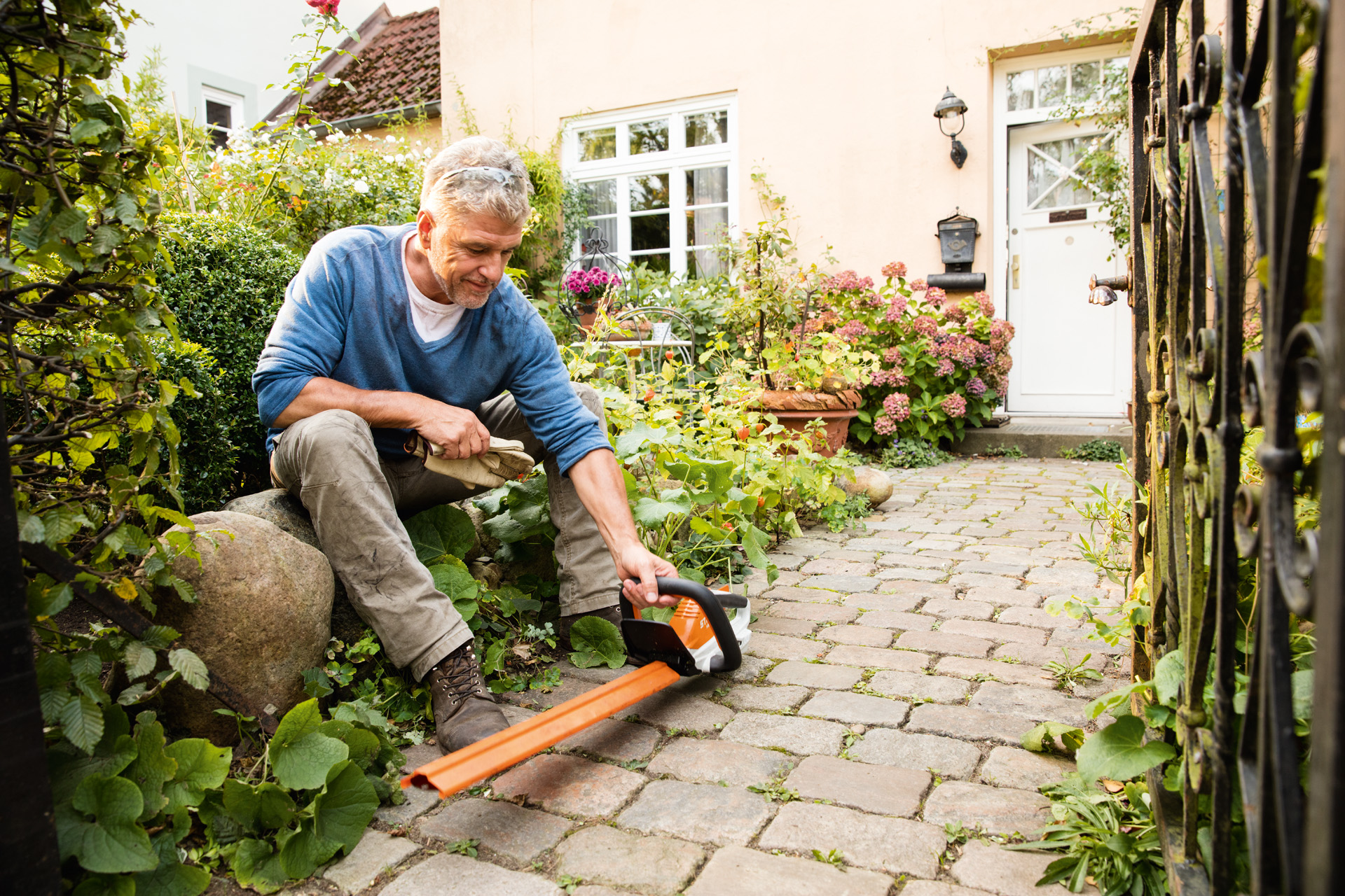 Muškarac sa STIHL električnim trimerom HSA 45 iz AI linije sedi ispred kuće